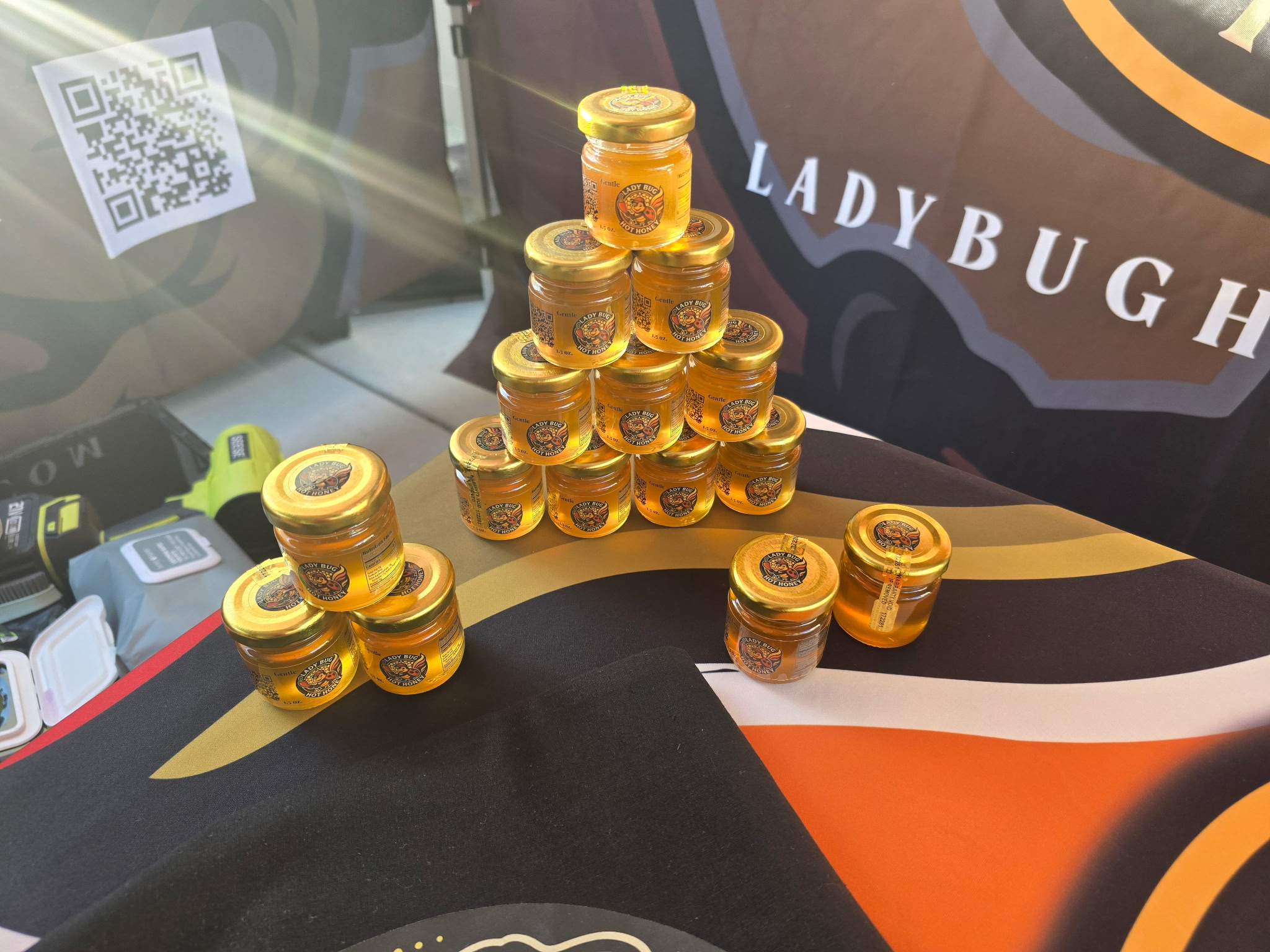 LadyBug Hot Honey booth at a Sacramento farmers market with banner, bottles, and free samples